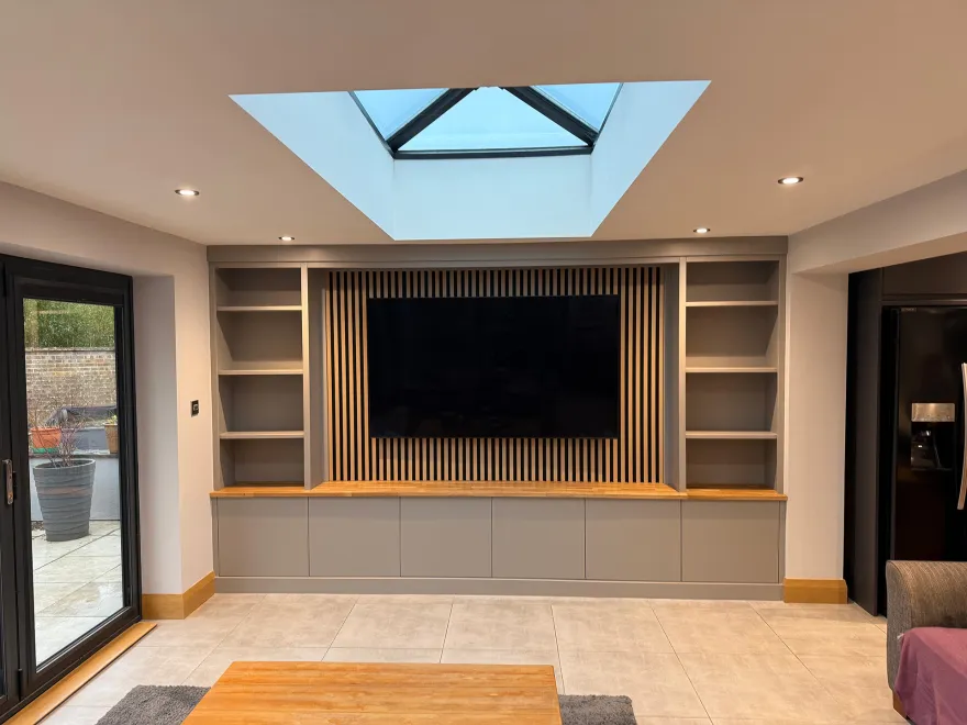 Grey media wall with a slatted timber TV panel, shelving and a roof lantern above