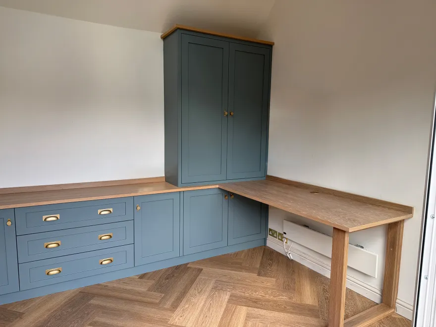 Blue-grey shaker base units and tall cupboard beside an oak L-shaped desk