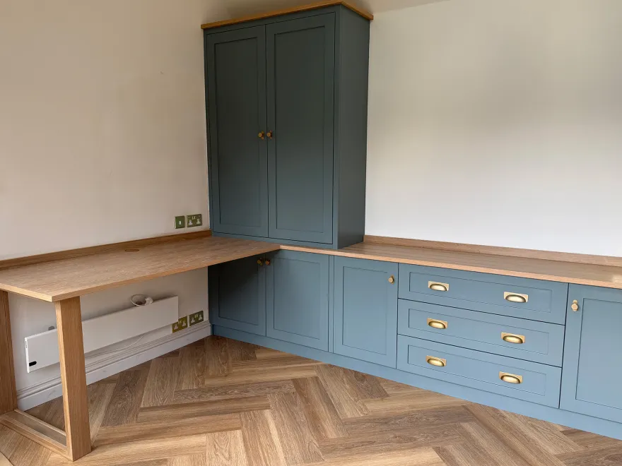 Corner of a blue-grey home office with an oak desk, drawers and tall cupboard
