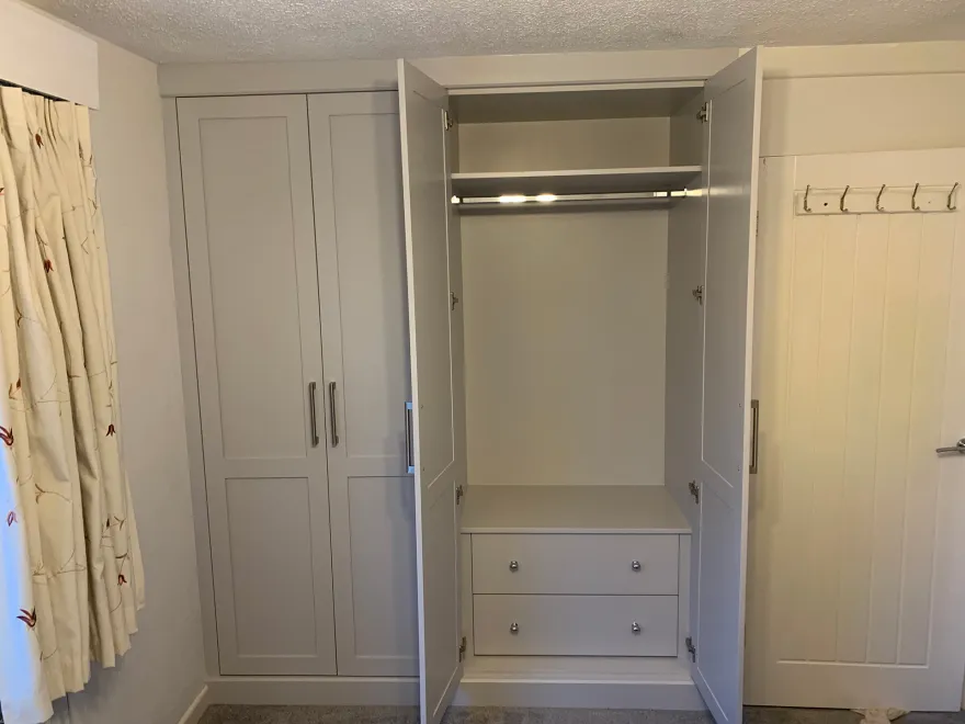Painted shaker fitted wardrobe open to show a lit hanging rail and drawers