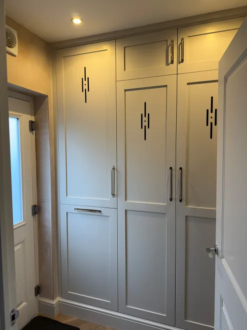 White painted boot room cupboards with decorative cut-out vents and chrome handles