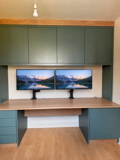 Green home office with twin monitors, an oak desk and wall cupboards above