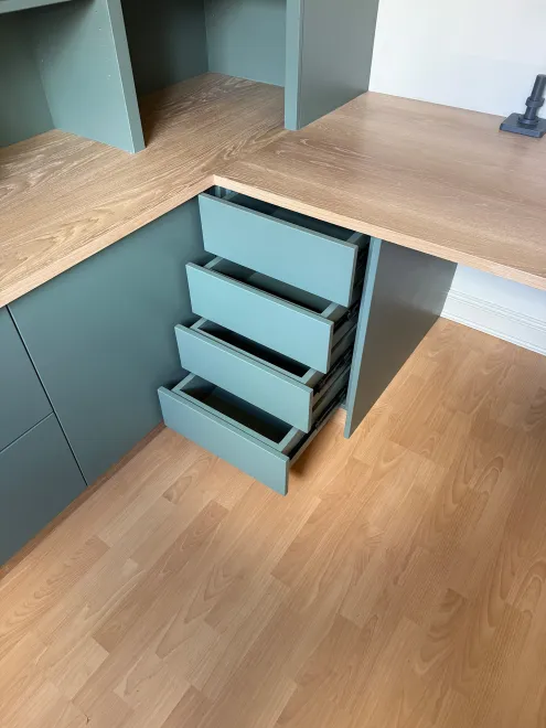 Green drawers pulled open beneath an oak corner desk in a home office