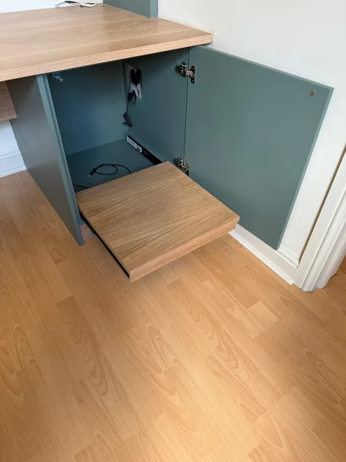 Pull-out oak platform inside a green desk cupboard with cable access