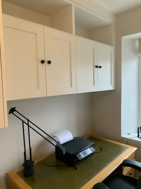 White shaker wall cupboards above an oak desk with a leather top