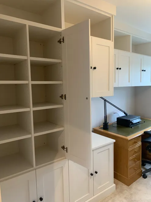 White office cupboard open to show adjustable shelving beside a desk