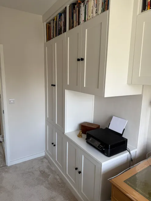 White fitted cupboards with a printer shelf and books stored above
