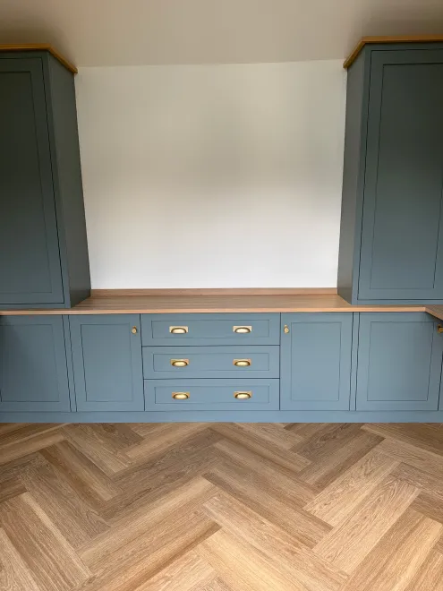 Tall blue-grey shaker cupboards framing a run of drawers and an oak worktop