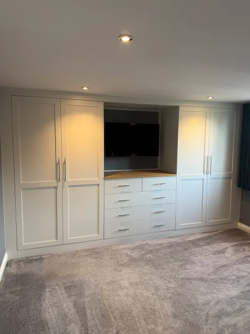Full-height view of fitted bedroom wardrobes framing a TV recess and drawer unit