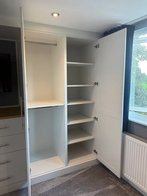 Open fitted wardrobe with a hanging rail and adjustable shelves beside a window