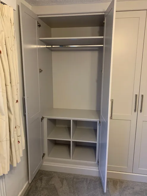 Open fitted wardrobe with a hanging rail above cubby-hole shoe storage
