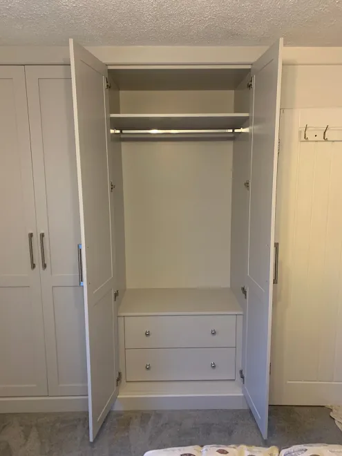 Painted shaker fitted wardrobe open to show a hanging rail, shelf and two drawers