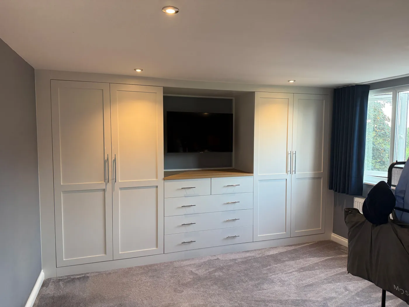 Pale painted fitted wardrobes either side of a TV recess with drawers below